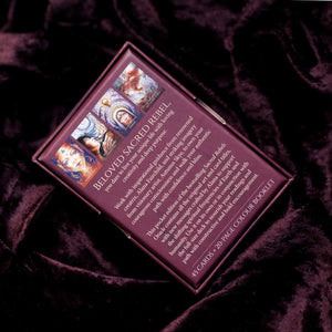 Card deck packaging with tarot card illustrations on a dark fabric background