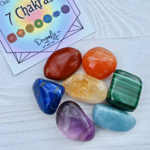 Set of colorful chakra stones with a '7 Chakras' card in the background on a white surface.