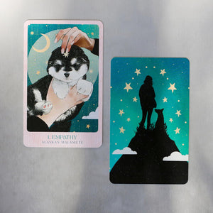 Two oracle cards featuring front illustration of card with a black and white dog, and back illustration with silhouette of a dog and person on a hill.