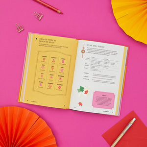 Open book with colorful pages on a pink background with decorative fans and a pen.