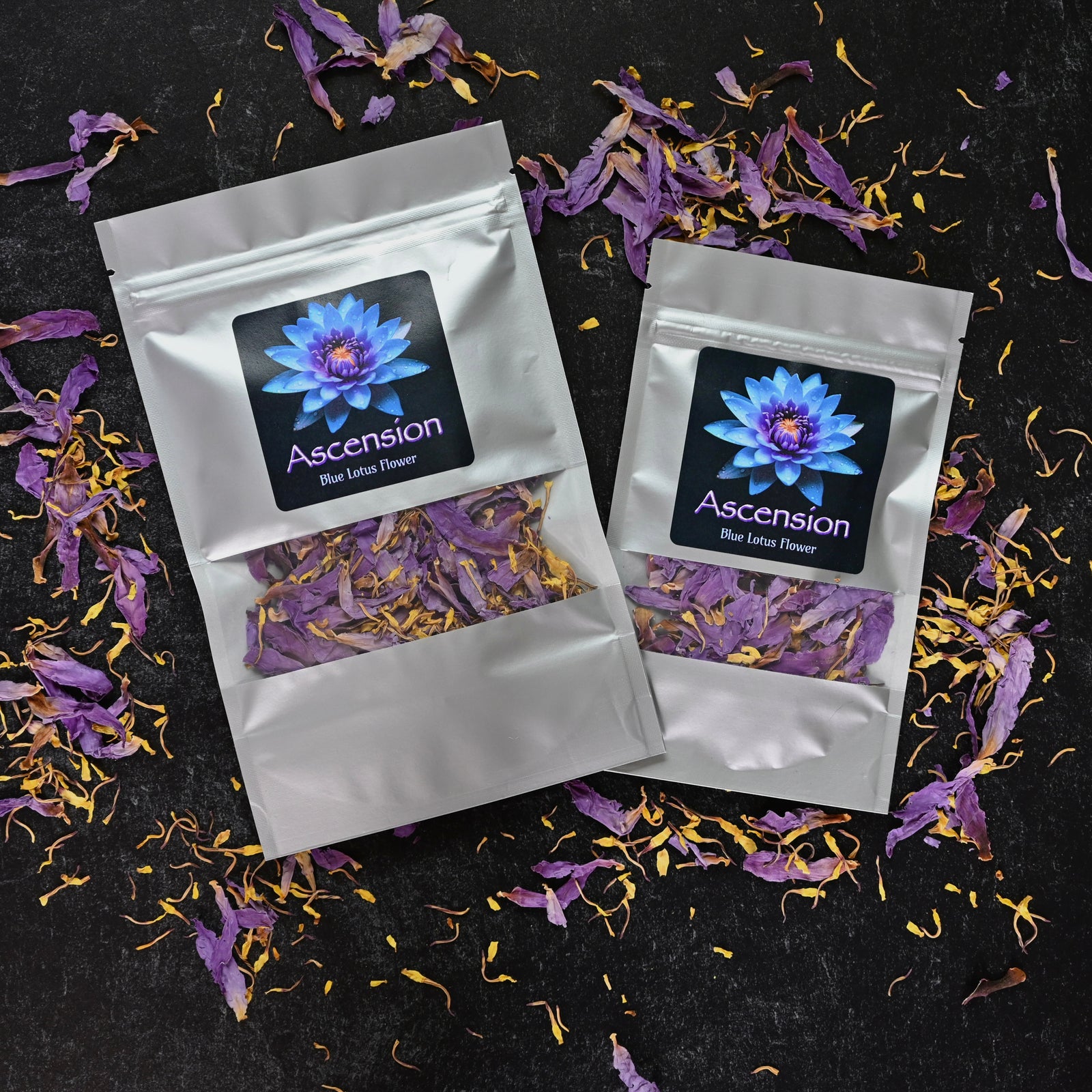 Two silver pouches of Ascension Blue Lotus Flower, with visible dried petals and a vibrant lotus label, surrounded by scattered petals on black background.
