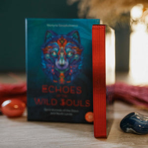 Oracle deck blurred in background with a colorful wolf design on the cover, on a wooden surface, with oracle cards showing red metallic edges.