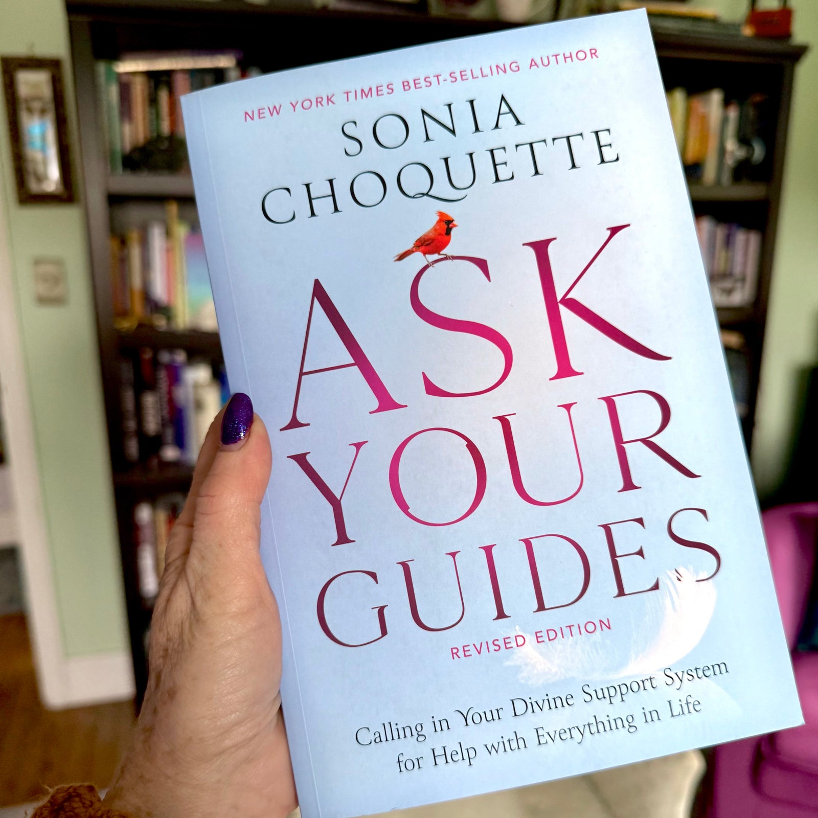 Book titled 'Ask Your Guides' by Sonia Choquette held in front of a bookshelf.