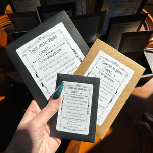 A hand holds a black envelope with a label that reads "There Are No Wrong Choices... 5 Card Mini Tarot Reading." This reading, provided by Dragonfly Art and Soul in Williamsville, NY, offers self-reflection, connection, and empowerment.