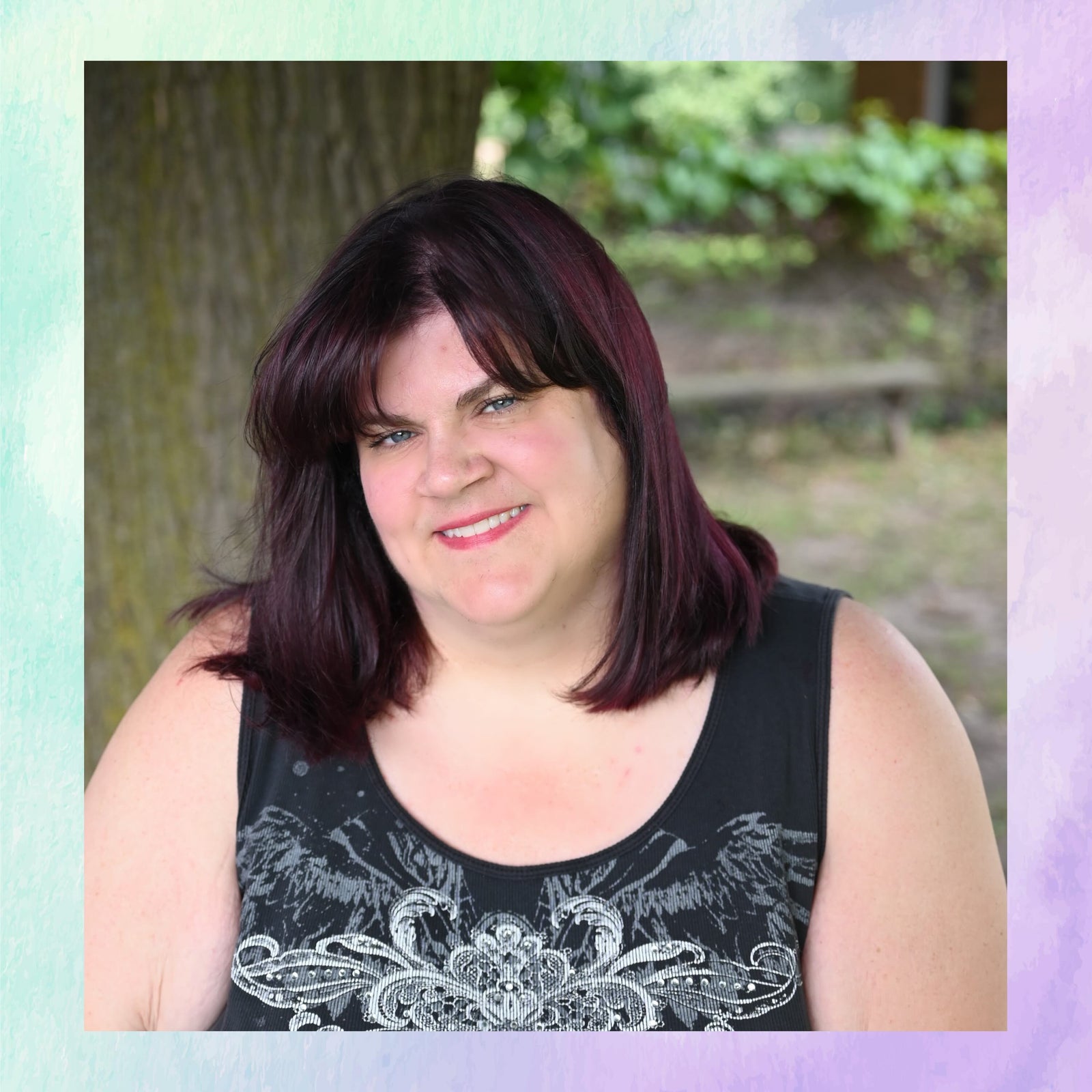 Woman with dark hair and a black sleeveless top standing outdoors with greenery in the background