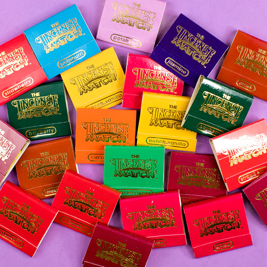An assortment of colorful Incense Matches matchbooks are scattered on a purple surface. The matchbooks come in various colors including red, yellow, green, purple, and gold, with fragrances labeled such as "French Vanilla," "Patchouli," "Sandalwood," and others to eliminate odors.