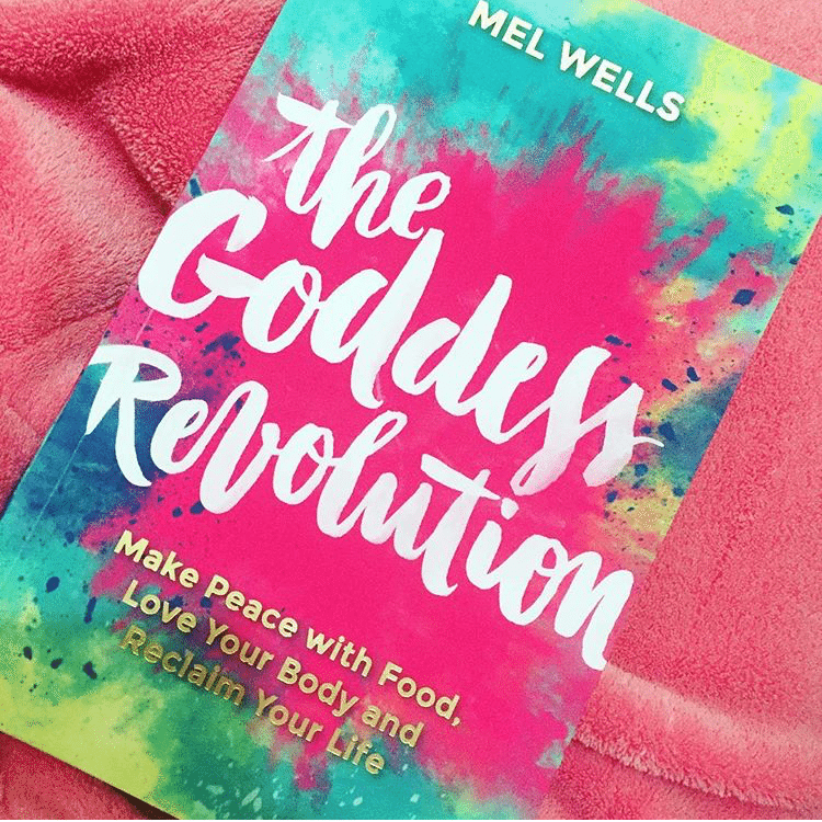 The image features the cover of the book "The Goddess Revolution" by Mel Wells. The cover design is vibrant and colorful, depicting a dynamic and bold graphic of the title in pink and green hues, which reflects the book's theme of promoting a positive body image and self-love.