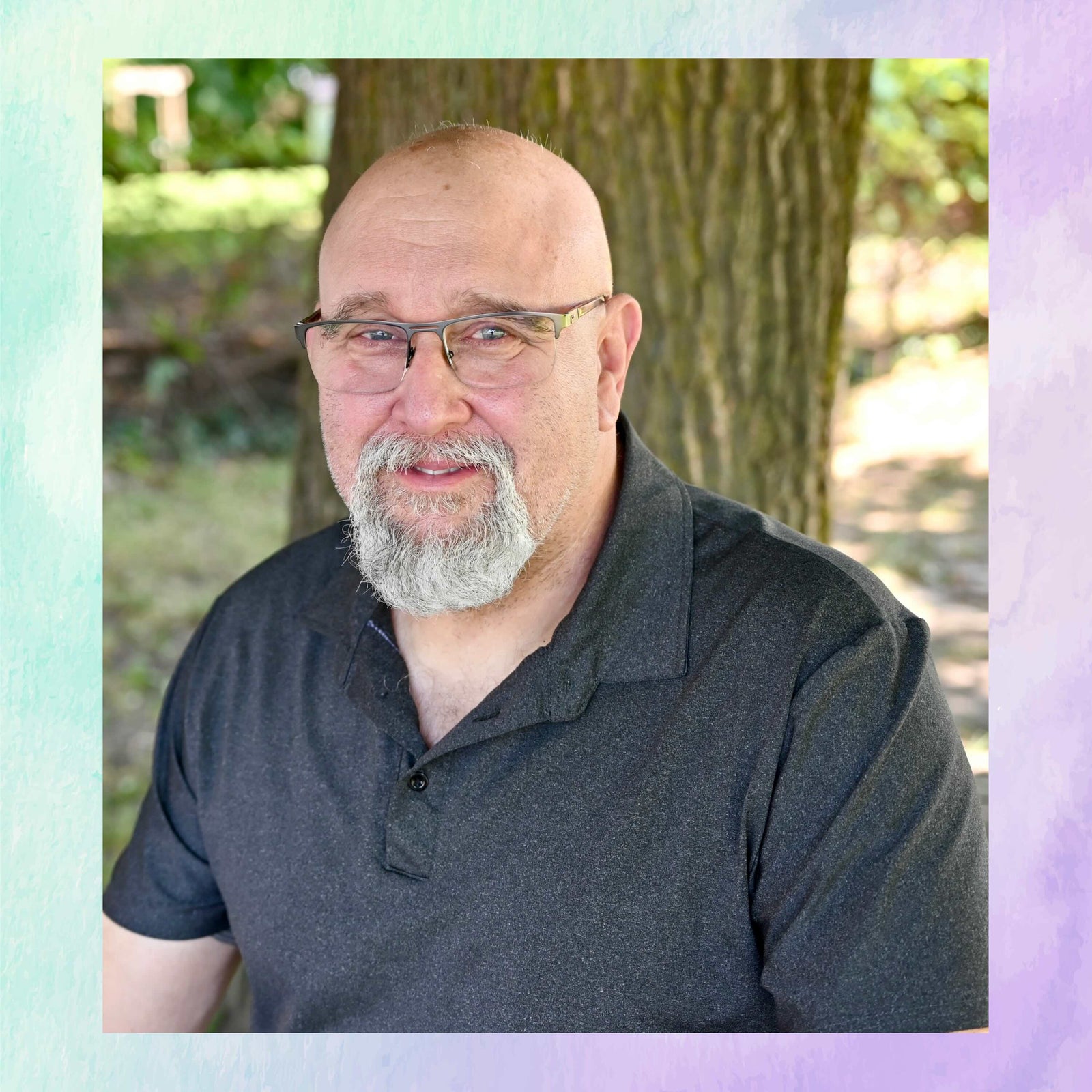 Man with glasses and a beard wearing a dark polo shirt outdoors.