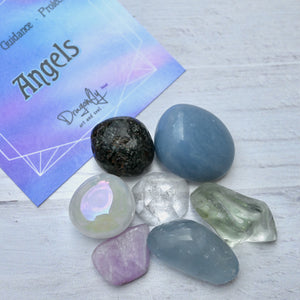 Set of crystals on a light wooden surface with a card labeled 'Angels' in the background.