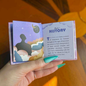 A hand holds a mini open book showing pages about 'Chapter 1 HISTORY' with an illustration of a silhouette under stars on a purple background.