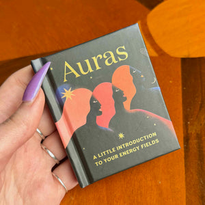 small Book titled 'Auras' held by a hand on a wooden surface