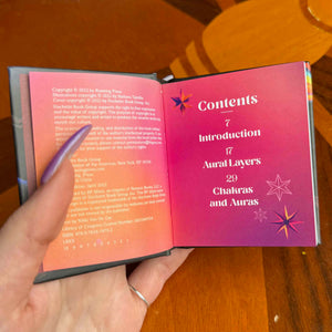 small Open book with a pink table of contents held by a hand on a wooden surface