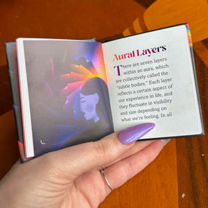 Hand holding a small open book with text about 'Aural Layers' on a wooden surface