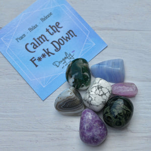 Colorful stones on a white surface with a blue card reading 'Calm the F**k Down'.
