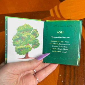 small book with a tree illustration and astrological information on a wooden surface