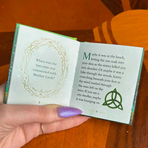 Hand holding a small open book with text and a green design on a wooden surface.