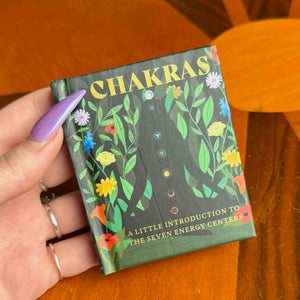 small Book titled 'Chakras' held by a hand on a wooden surface