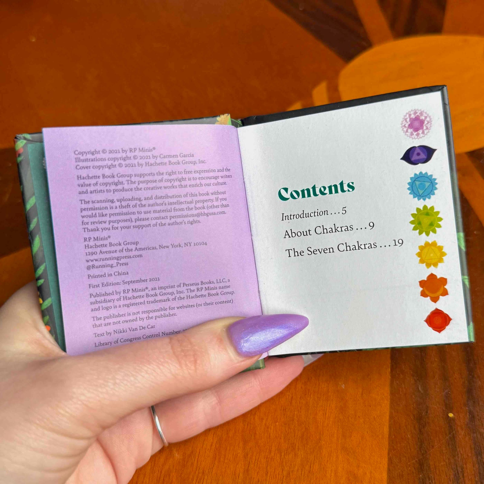 small Book titled 'Chakras' held by a hand on a wooden surface