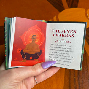 small Book titled 'The Seven Chakras' held open by a hand on a wooden surface