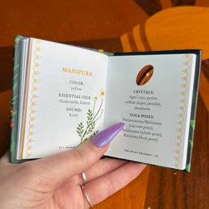 Hand holding an small open book with information about Manipura chakra on a wooden surface