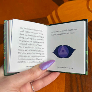 small Open book with text and an eye illustration held by a hand on a wooden surface