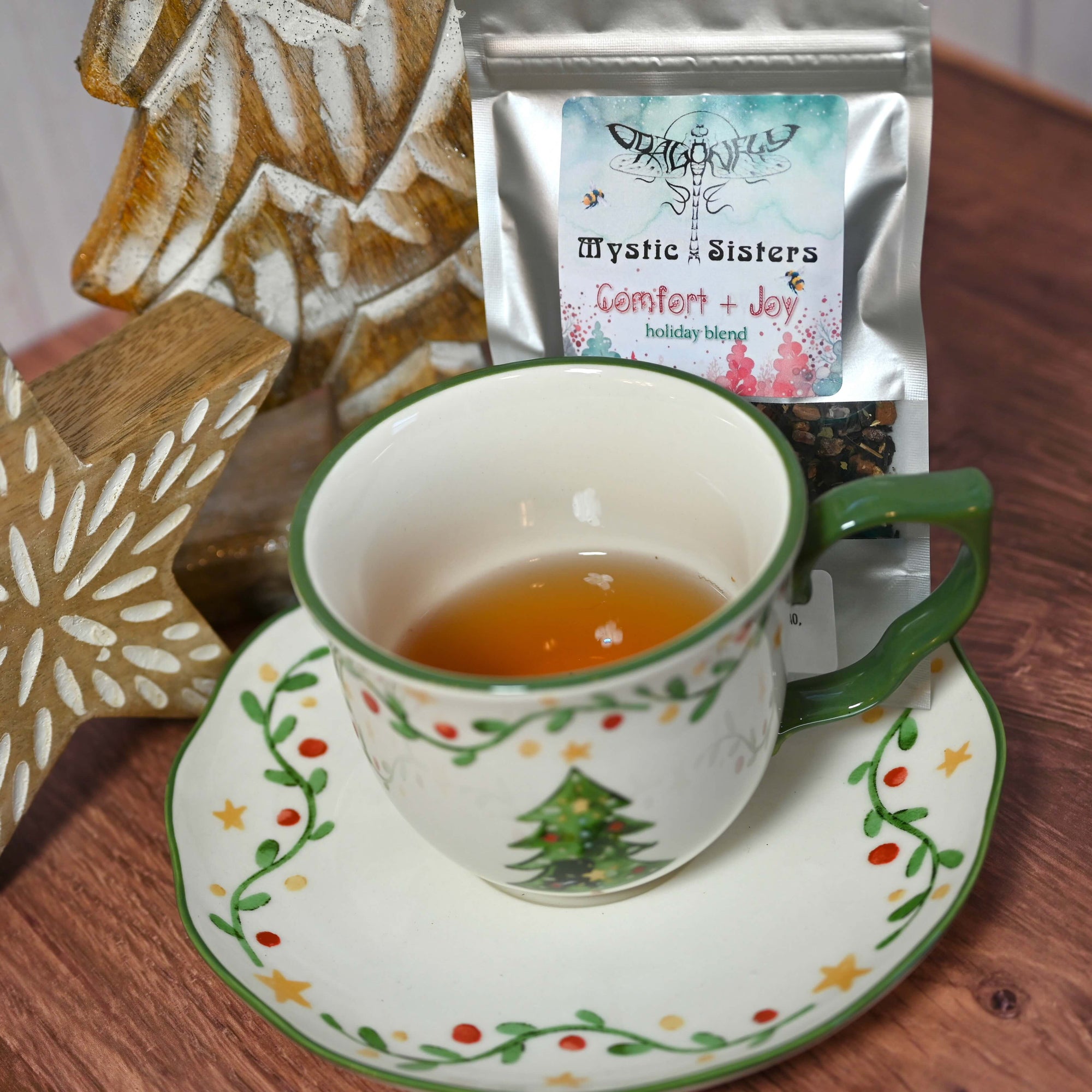 Tea cup with festive design on a wooden table next to a bag of 'Mystic Sisters' tea.