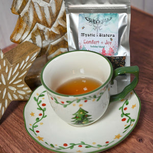 Tea cup with festive design on a wooden table next to a bag of 'Mystic Sisters' tea.