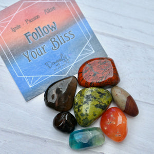 Colorful stones on a wooden surface with a card reading 'Follow Your Bliss'.