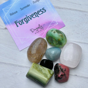 Colorful stones on a light wooden surface with a card reading 'Forgiveness' and 'Release Surrender Accept'.