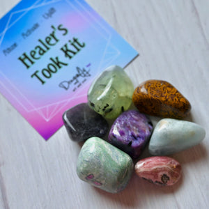 Colorful stones on a white surface with a 'Healer's Took Kit' book in the background.