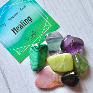 Colorful crystals on a white surface with a green card labeled 'Healing'.