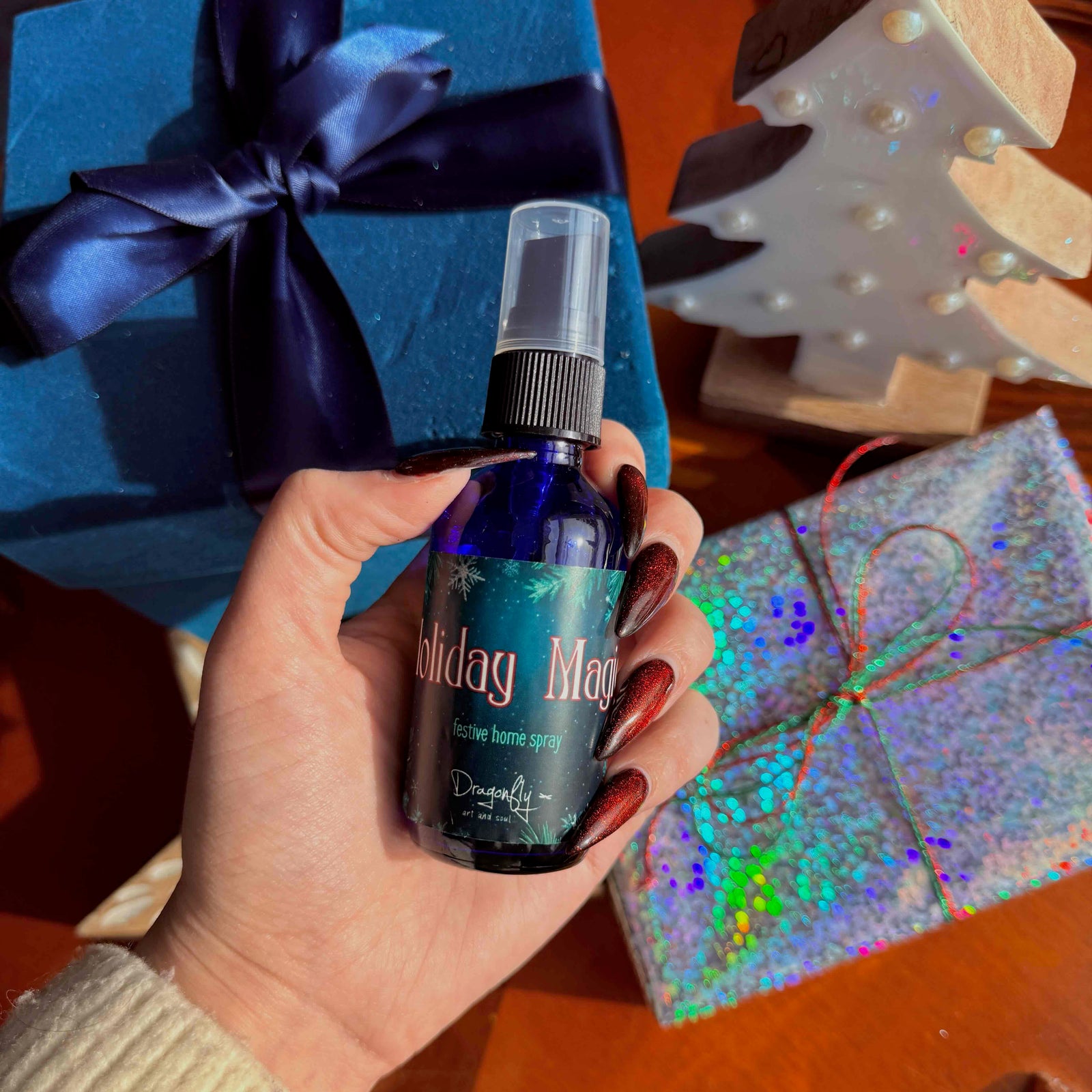Hand holding a 'Holiday Magic' spray bottle with festive background