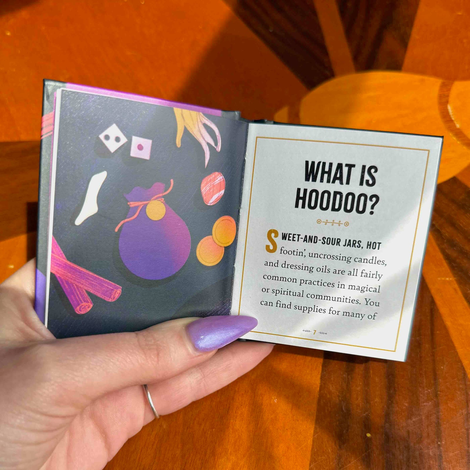 Hand holding a book titled 'Hoodoo: A Little Introduction' by Donyae Coles on a wooden surface.