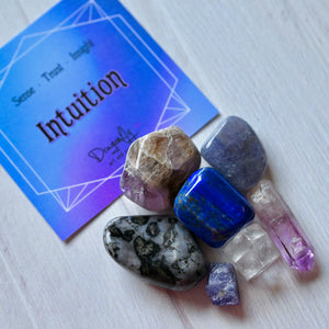 Crystal stones on a white surface with a card labeled 'Intuition' in the background.