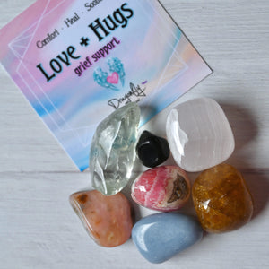 Colorful stones on a card with 'Love + Hugs' text on a light background