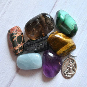Collection of various colorful stones and a small metal angel metal on a white wooden surface.