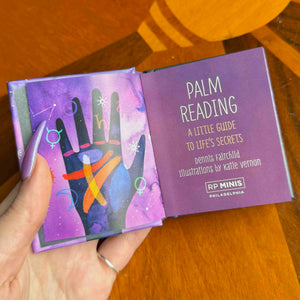 small Purple book titled 'Palm Reading' held by a hand on a wooden surface