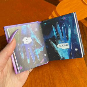 small Open book with artistic illustrations of hands and text on a wooden surface