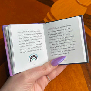 Hand holding a small open book with text and a small illustration on a wooden surface