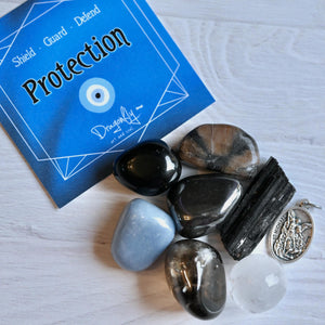 Collection of stones and a pendant on a white surface with a 'Protection' card in the background.