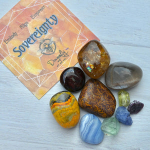 Collection of polished stones with a card featuring 'Embody Aligned Empower Sovereignty' on a light wooden surface.