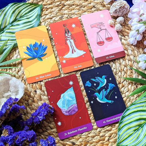 Set of oracle cards with colorful designs on a woven surface with plants and stones.