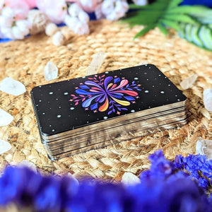 Set of oracle cards with a colorful flower design on a woven mat with flowers and crystals.
