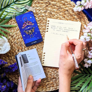 Person holding a pen and open book on a woven mat with decorative elements