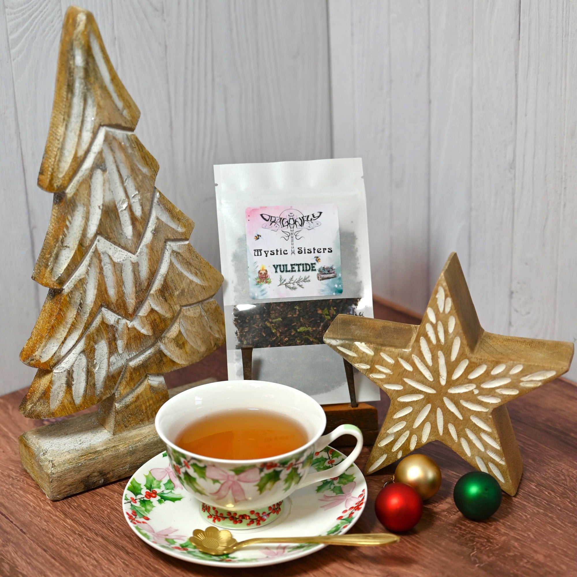 Tea cup with saucer, wooden Christmas tree, and star decoration on a wooden surface.