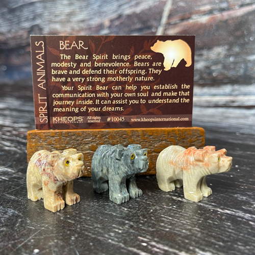 Three small bear figurines, crafted from differently colored stones, are displayed in front of a card. The card reads: "The Bear Spirit brings peace, modesty and benevolence. Bears are brave and defend their offspring. They have a very strong motherly nature." Each Spirit Animal holds a unique meaning as your spirit animal.