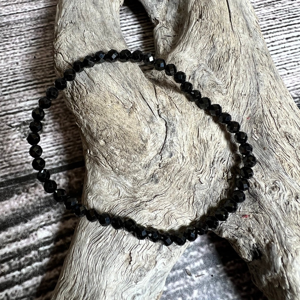 A black faceted beaded spinel bracelet laid out on a wooden surface.