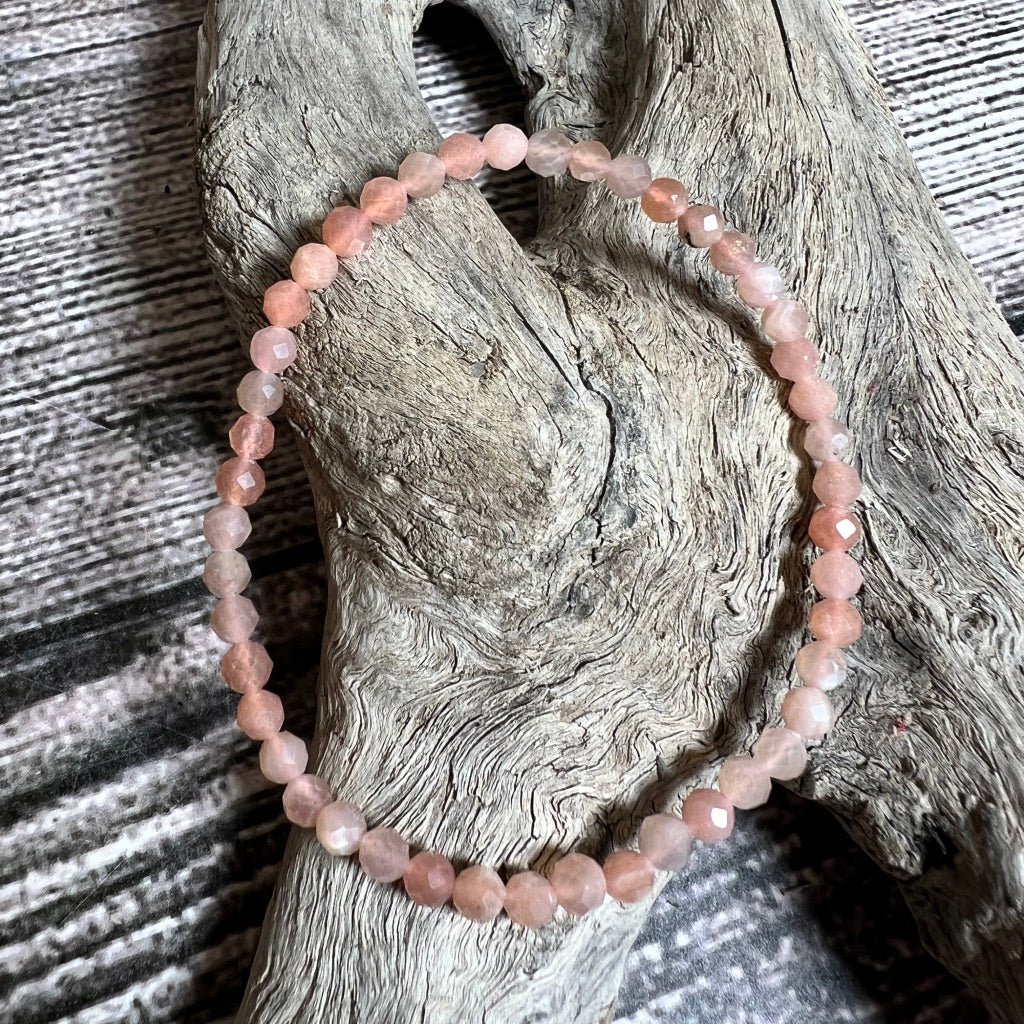 A stretchy bracelet made of orange pink faceted sunstone beads, displayed on a wooden surface.