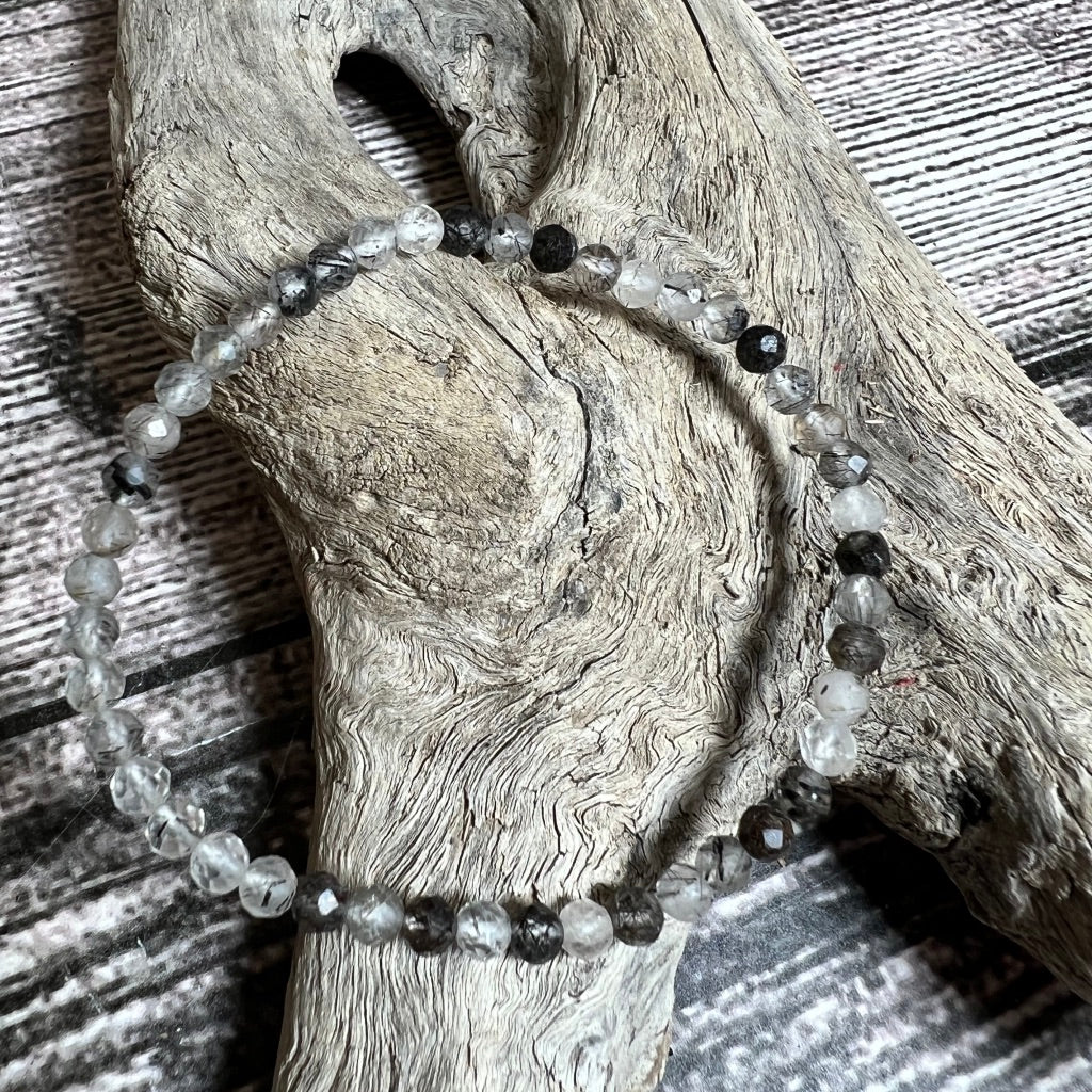 A black and clear faceted beaded tourmaline in quartz bracelet laid out on a wooden surface.