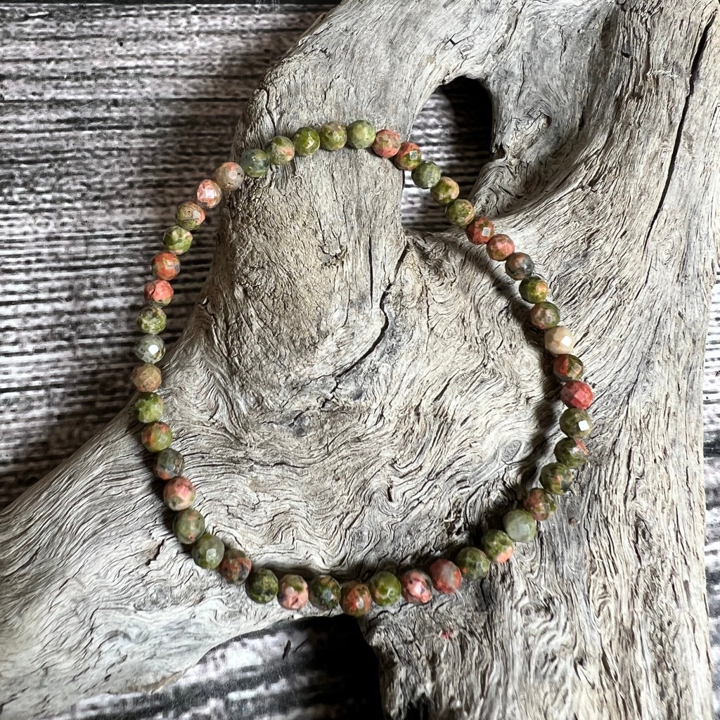 A green and orange faceted beaded Unakite bracelet displayed on a wooden surface.